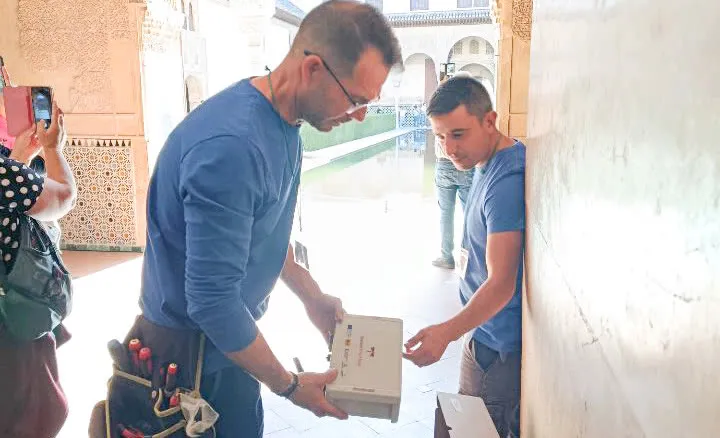 Dos técnicos manipulan un equipo de medida en una galería de patio de la Alhambra, con una fuente al fondo
