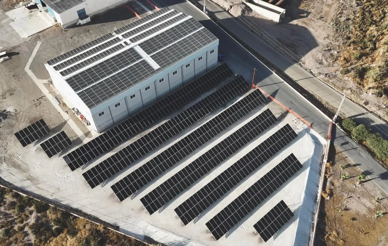 Vista aérea de una nave industrial con paneles solares en la cubierta y seis filas de paneles sobre el suelo contiguo